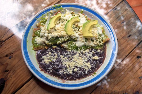 Chilaquiles with salsa verde, cotija cheese, crema, onion and avocado, and a side of refried black beans
