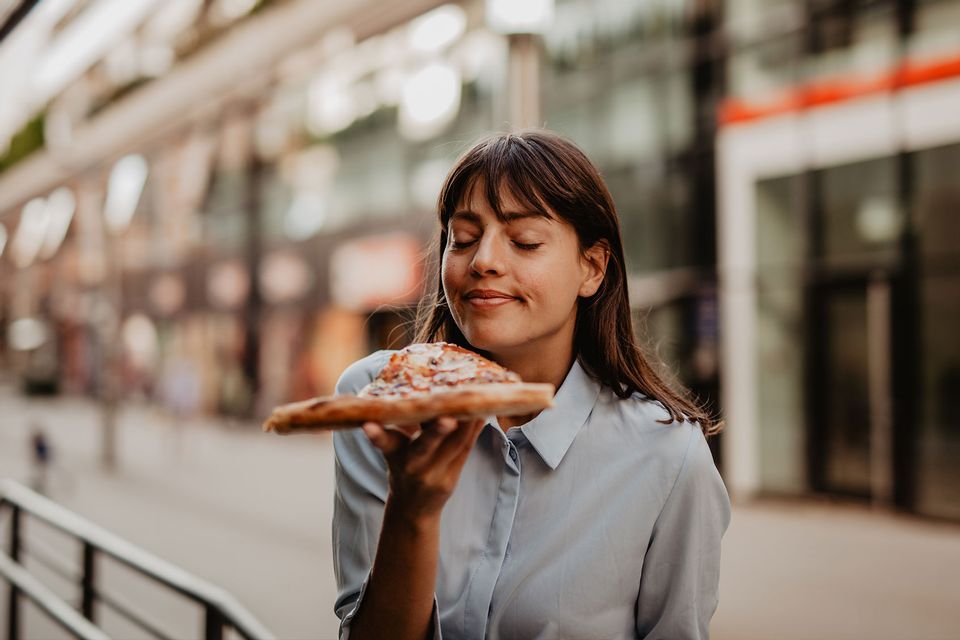 Portrait of a young woman smelling and about to taste a pizza slice.